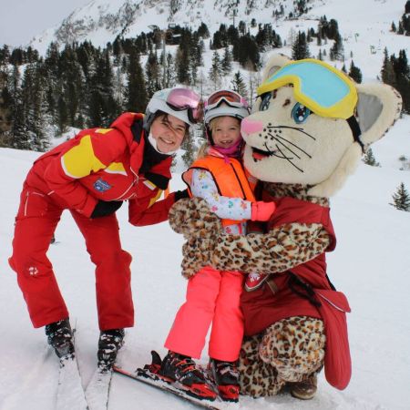 Skischülerin der Skischule Krallinger auf dem Schoß von Maskottchen Kiki